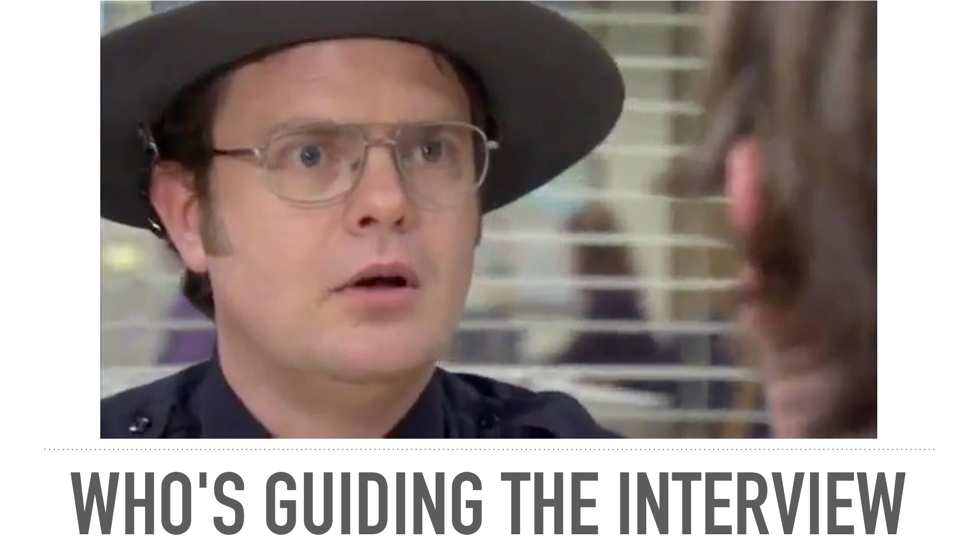 A man in glasses and a cowboy hat expressing surprise or concern while looking to the right in an office setting with blinds. Slide text reads 'WHO'S GUIDING THE INTERVIEW.'
