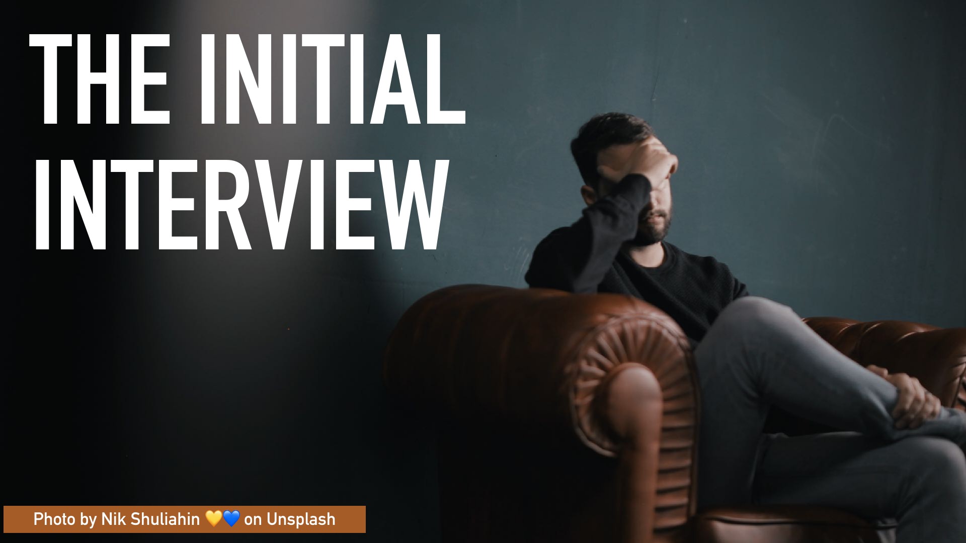 A bearded man in dark clothing sits pensively on a leather chair with his hand on his face against a teal background. The slide is titled 'THE INITIAL INTERVIEW' in large white text. Photo by Nik Shuliahin on Unsplash.