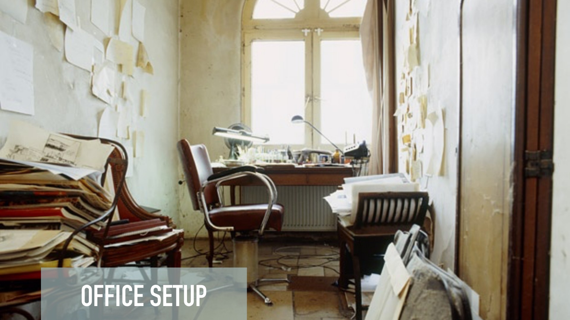 A vintage office workspace titled 'Office Setup' features minimal wooden furniture, scattered papers and sketches on cream walls, a desk with task lighting near tall windows, and documents arranged throughout, suggesting a creative or design-focused environment with natural light flooding the minimalist interior.