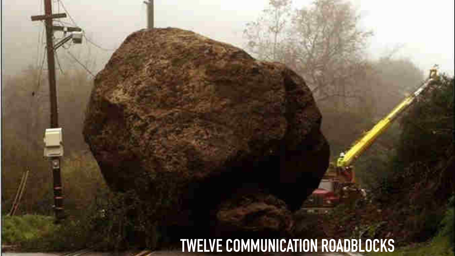 A massive, moss-covered boulder sits centered on a forest road, completely blocking passage. Utility poles and yellow metal infrastructure frame the scene; bare trees fade into mist. The slide title reads 'TWELVE COMMUNICATION ROADBLOCKS.'
